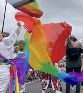 Photo of rainbow coloured material in the foreground of a Pride flag